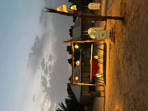 Desert camp at dusk with glowing lanterns, canopy and sandy ground under pastel sky