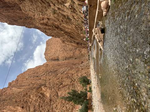 Narrow canyon walls of Todra Gorge tower above shallow stream and stone riverbed