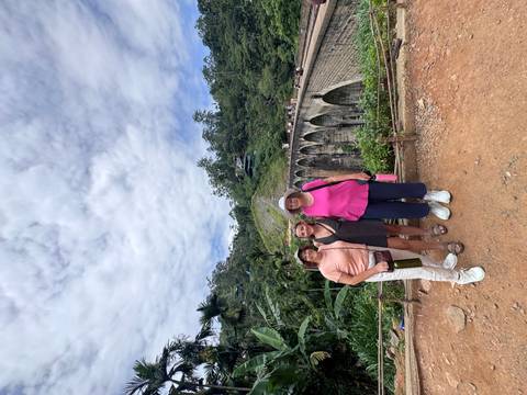Three women pose in front of Sri Lanka’s Nine Arches Bridge with jungle scenery and cloudy sky