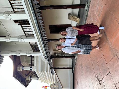 Three women dressed modestly stand barefoot outside the ornate white Temple of the Tooth in Kandy