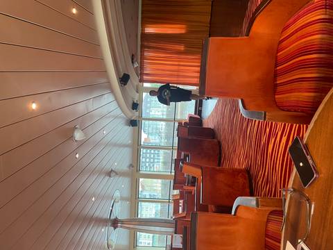 Interior lounge of a cruise vessel with warm wooden furnishings and a man walking past large windows