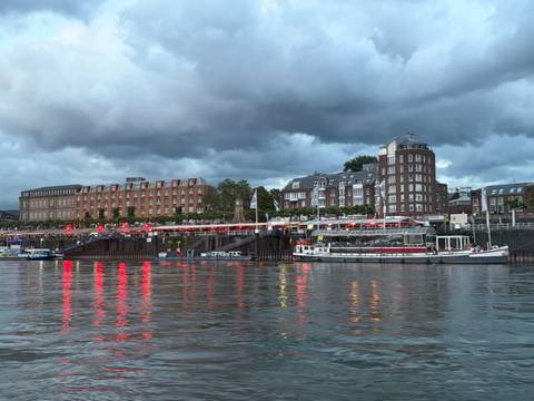 Riverside cityscape at dusk with restaurant lights reflecting red on the water beside moored boats