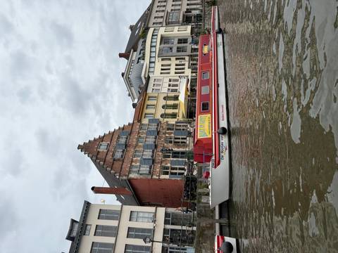 Canal-side row of historic buildings with red and yellow tour boat moored in front under cloudy sky