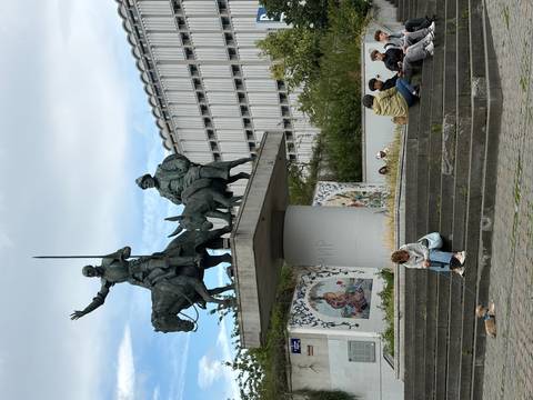Bronze statue of Don Quixote and Sancho Panza on horseback in a public square with people sitting nearby