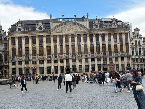 Broad view of the ornate guildhall on Brussels’ Grand Place with crowds of tourists and locals in the square.