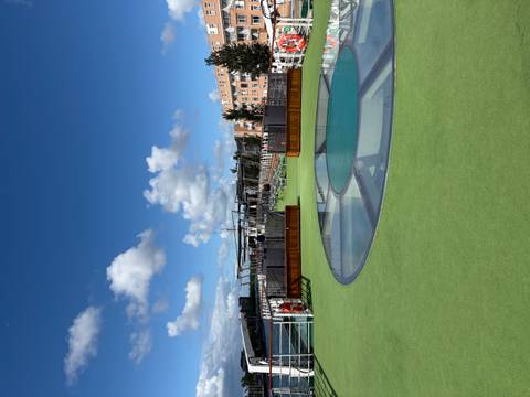 Open sundeck on a cruise vessel featuring artificial turf, skylights and clear blue skies dotted with small clouds.