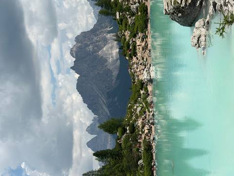 Stunning turquoise alpine lake framed by rugged Dolomite peaks with hikers dotted along the rocky shoreline.
