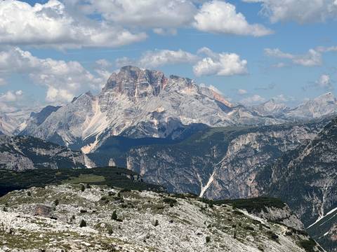 Panoramic view of jagged Dolomite summit with forested valleys and scattered clouds above.