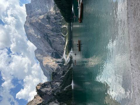 Crystal clear lake with rowboats and towering Dolomite cliffs reflected in the still water.