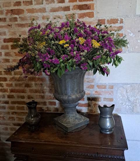 Large pewter urn filled with purple and yellow flowers against an old brick wall