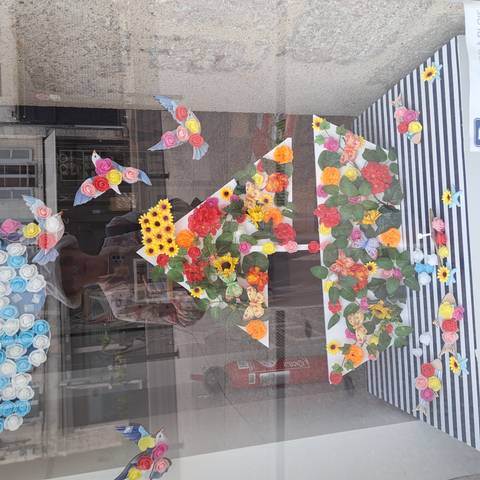 Storefront window art with colourful paper flowers and reflected image of the photographer