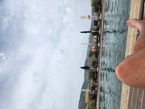 View over a serene infinity pool with loungers and distant hills, foreground shows traveller’s legs