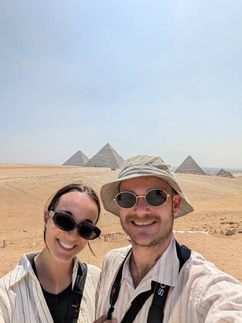 Couple selfie with the pyramids rising from the desert plateau behind them