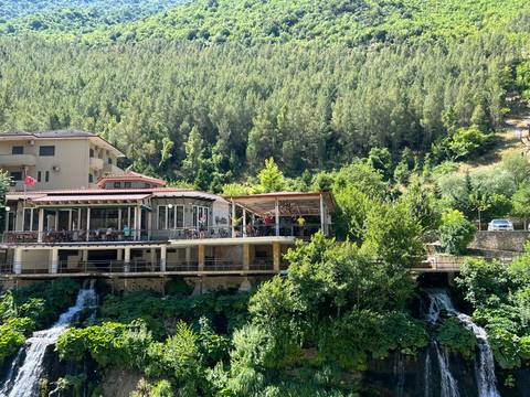 Hillside restaurant complex overlooks a lush valley with small cascades and dense pine forest.