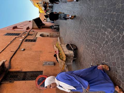 Narrow ochre alley with a fruit cart and locals walking past rustic walls in the medina.