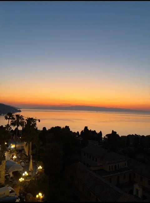Brilliant orange sunset over the Mediterranean Sea with silhouetted palms and headland