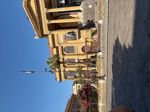 Historic Teatro Massimo opera house with Italian flag and palm trees under clear sky