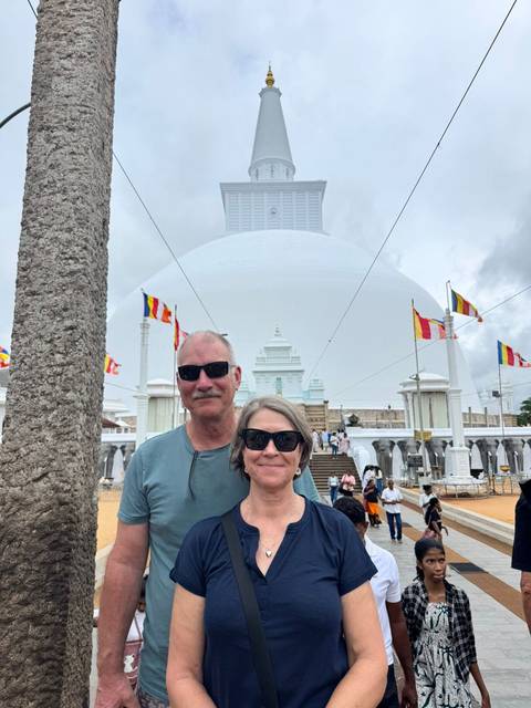 A couple stands before a large white Buddhist stupa adorned with colorful flags