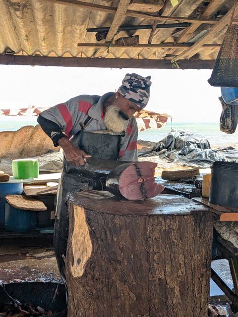 Fisherman with a white beard cuts a large tuna on a wooden block by the seaside