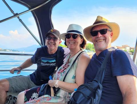 Three cheerful travellers in hats enjoying a boat ride on a sunny lake.