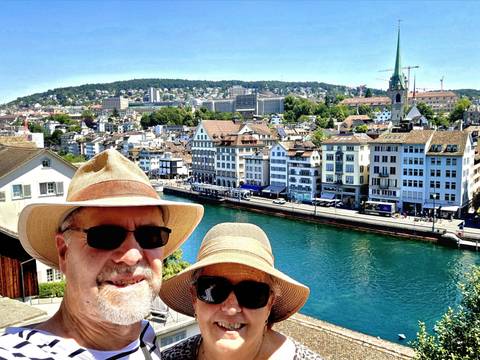 Selfie of couple wearing hats with Zurich’s old town and turquoise river behind.