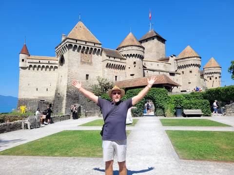 Traveller with arms raised in front of medieval Chillon Castle on Lake Geneva.