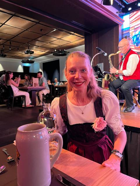 Smiling woman in traditional dress holding a drink while musicians perform on stage behind.