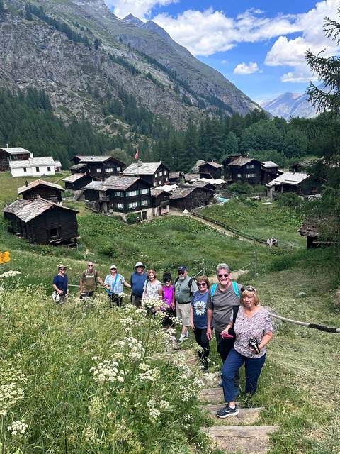 Hiking group overlooking a picturesque cluster of rustic alpine cabins in a green valley.