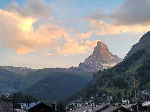 Iconic Matterhorn peak glowing in warm sunset light above verdant valleys.