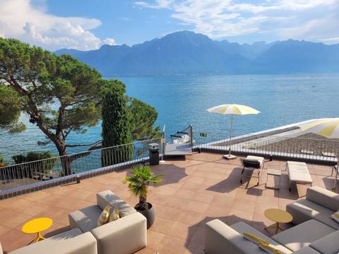 Terrace with loungers and yellow umbrellas overlooking a tranquil blue lake and mountains.