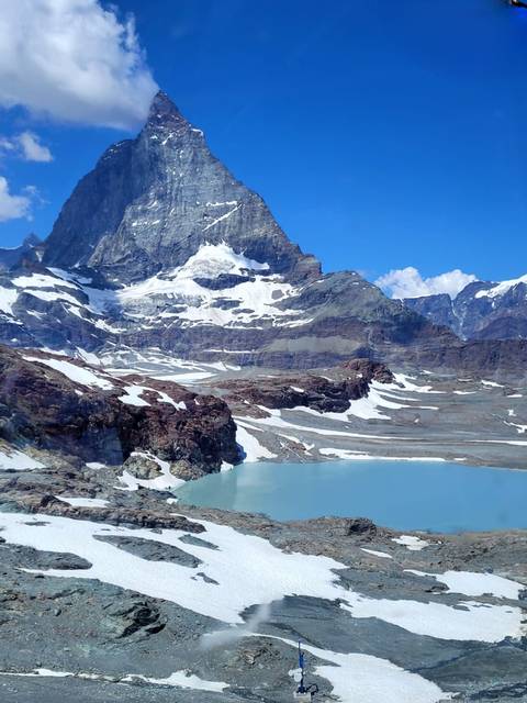 Turquoise glacial lake beneath the snowy Matterhorn surrounded by rugged ridges.