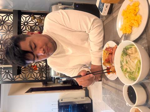 Man eats breakfast with chopsticks at a restaurant table set with soup and eggs.