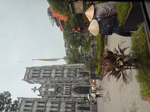 Street view of St. Joseph’s Cathedral with tourists in conical hats and surrounding greenery.