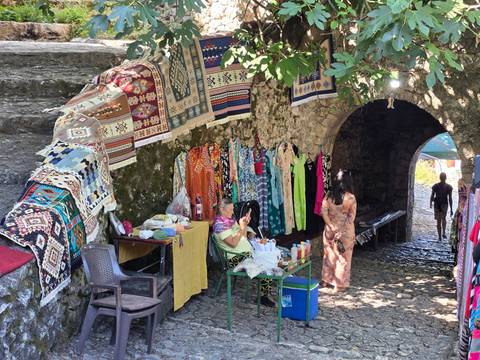 Market stall under stone arch selling colourful textiles and dresses in a Bosnian old town.