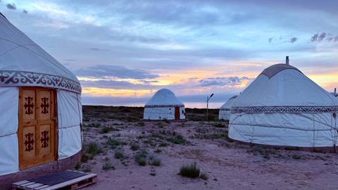 Traditional white yurts scattered across a barren steppe at colourful sunset.