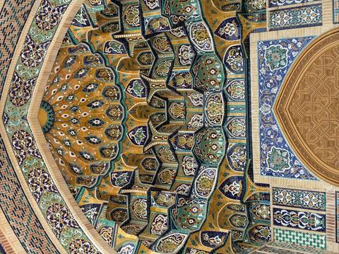 Intricate Islamic tilework ceiling inside a historic madrasah with rich blues, yellows and geometric patterns.