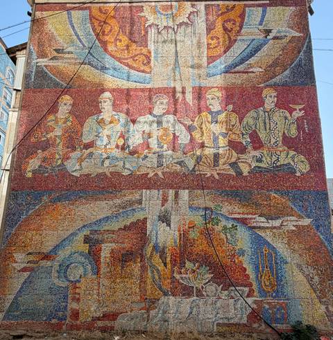 Colorful Soviet-era mosaic mural depicting figures with goblets and industrial themes.