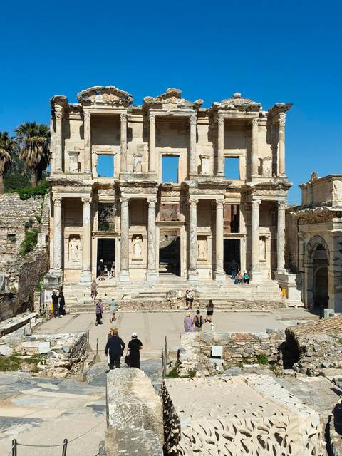 Grand marble façade of the Library of Celsus rises above visitors exploring the ancient ruins.