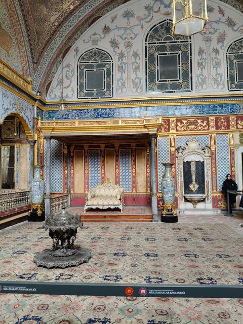 Ornately decorated throne room with gilded columns, patterned tiles and a single guard.
