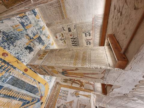 An ornately painted stone pillar stands in the middle of a richly decorated burial chamber.