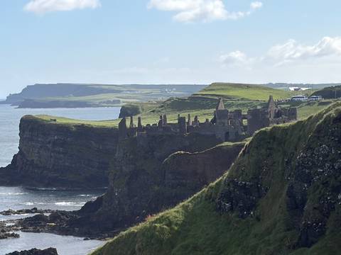Ruins of Dunluce Castle perched on dramatic green cliffs above the Atlantic with layered headlands beyond.