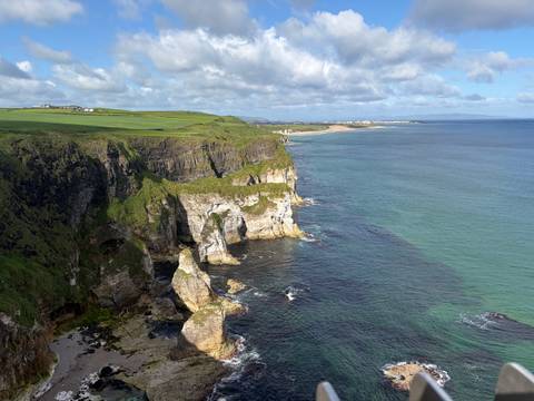 Expansive aerial view of rugged green cliffs meeting turquoise sea under a partly cloudy sky.