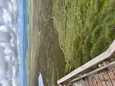 Wide open moorland and rolling hills stretch to the horizon under patchy clouds, seen from a wooden railing viewpoint.