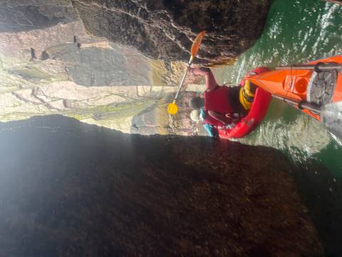Kayakers paddle through a narrow sea cave corridor between towering rock walls.