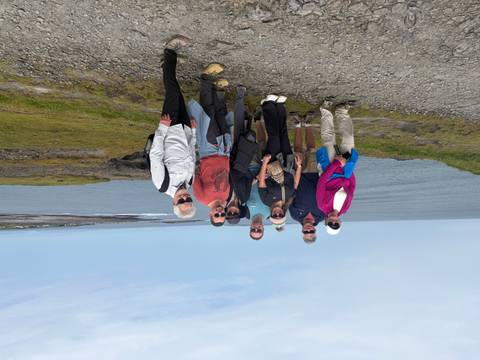 Group of travellers stands on rocky coastal path with sweeping sea views under light blue sky.
