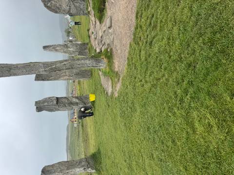 A caretaker tends the ancient standing stones of Callanish on a misty grass plain.