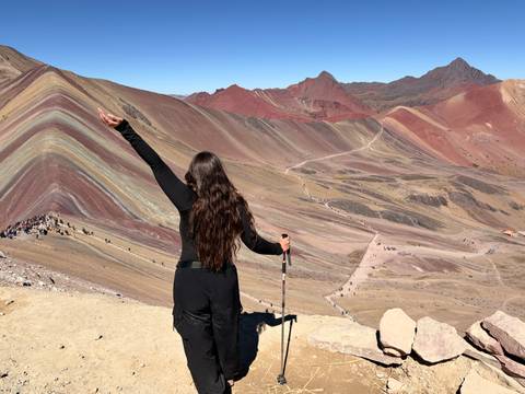 A woman triumphantly raises her arm at the colourful striped slopes of Rainbow Mountain in Peru.