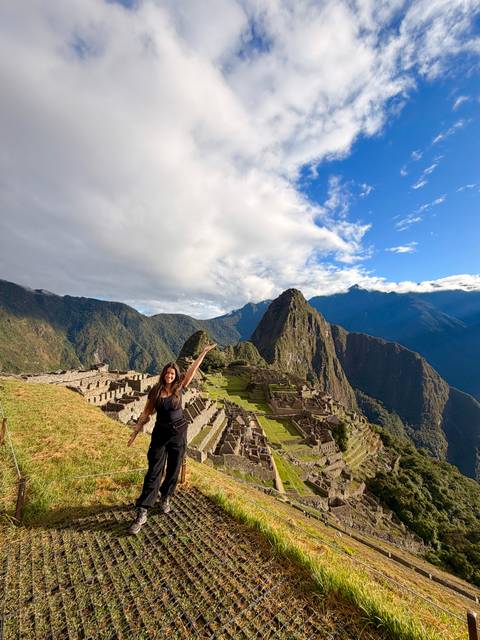Panoramic view of Machu Picchu ruins framed by dramatic green peaks under a partly cloudy sky.