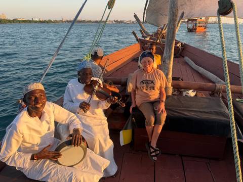 Small group enjoys music on a wooden dhow at sea during warm sunset light.