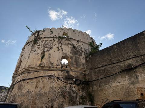 Weathered round tower of an old fort rises against a clear blue sky with greenery sprouting from cracks.